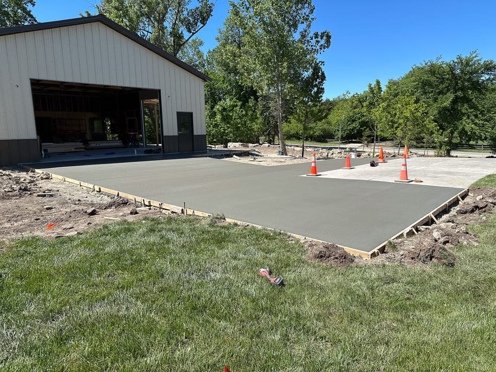 big outdoor shed with a concrete driveway leading up to it with freshly poured concrete